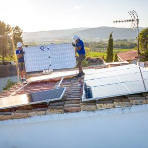 ouvriers installant des panneaux solaires sur le toit d'un bâtiment à la campagne, avec des vignes en arrière plan.