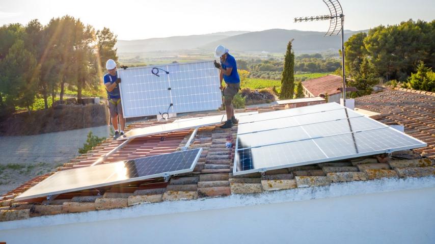 ouvriers installant des panneaux solaires sur le toit d'un bâtiment à la campagne, avec des vignes en arrière plan.